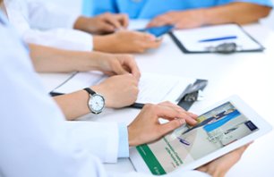 Doctor using tablet computer at medical meeting, closeup. Group of colleagues at the background.